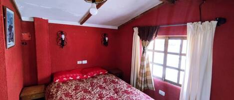A room with a bed, a window with curtains, a wall-mounted light fixture, and a ceiling fan.