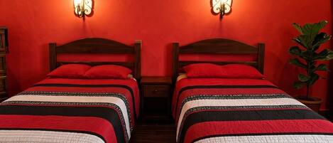 Una habitación con dos camas, cada una con una colcha estampada en rojo y negro, cabeceros de madera y lámparas fijadas a la pared.