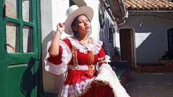Una persona vestida con traje tradicional frente a un edificio con puerta verde y paredes blancas.