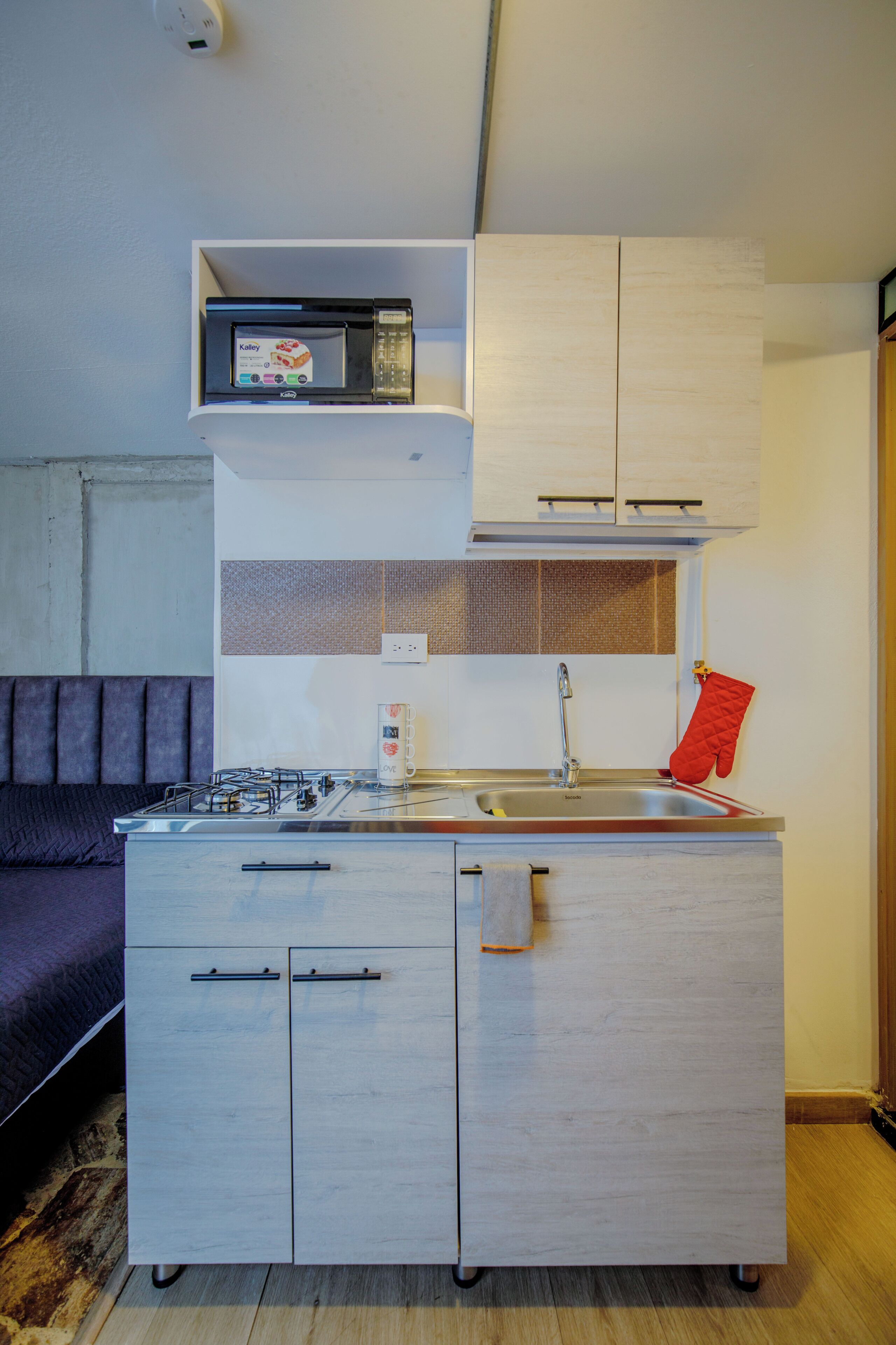 Una kitchenette compacta con microondas, estufa y lavamanos.