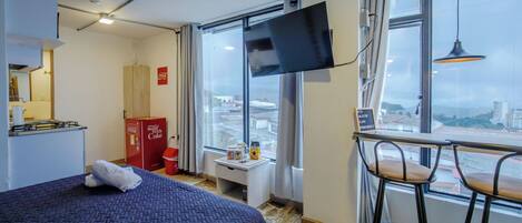 A hotel room with a bed, a desk with a chair, a television, and a window with a view of the city.