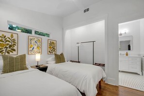 Ein Hotelzimmer mit zwei Betten, einem Nachttisch mit Lampe, einem Kleiderschrank und einem Badezimmer mit Spiegel und Waschbecken.