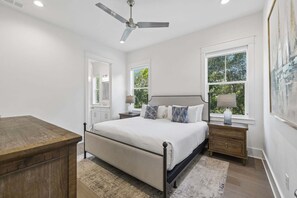 A bedroom with a bed, bedside tables, a ceiling fan, and a window with a view of greenery. - Easy Walk 2 Beach! Private Pool, LSV/Golf Cart & Bikes! (Santa Rosa Beach)