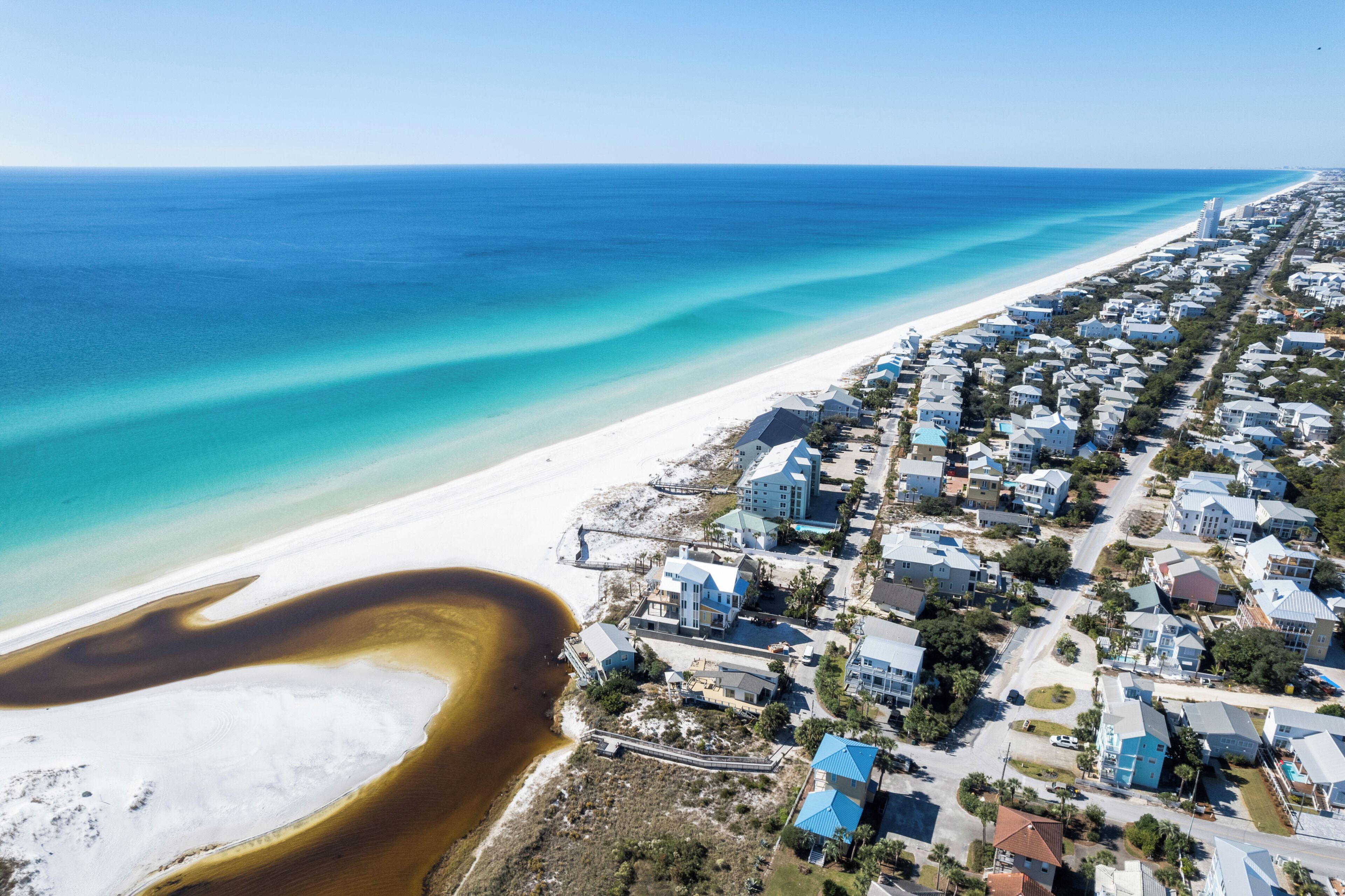 Vista aérea de uma área residencial costeira com casas, uma praia e um oceano azul e límpido.