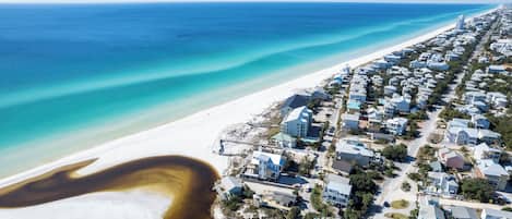 Vista aérea de uma área residencial costeira com casas, uma praia e um oceano azul e límpido.