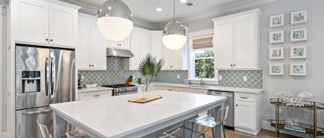 A modern kitchen with stainless steel appliances, a marble island, and pendant lighting.