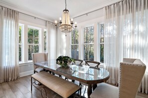 Ein Esszimmer mit Tisch mit Glasplatte, gepolsterten Stühlen und einer Bank, beleuchtet von einem Kronleuchter.