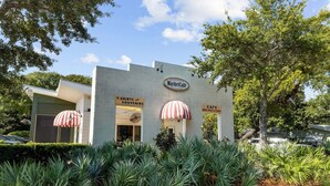 A building with a sign for 'Market Café' and 'T-Shirts and Souvenirs' with two red and white striped umbrellas. - NEW! EZ Walk to Beach! Private Pool, LSV/Golf Cart, & Bikes! (Santa Rosa Beach)