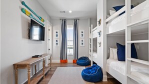 A modern bedroom with bunk beds, a flat-screen TV, and a wooden bench. - NEW! EZ Walk to Beach! Private Pool, LSV/Golf Cart, & Bikes! (Santa Rosa Beach)