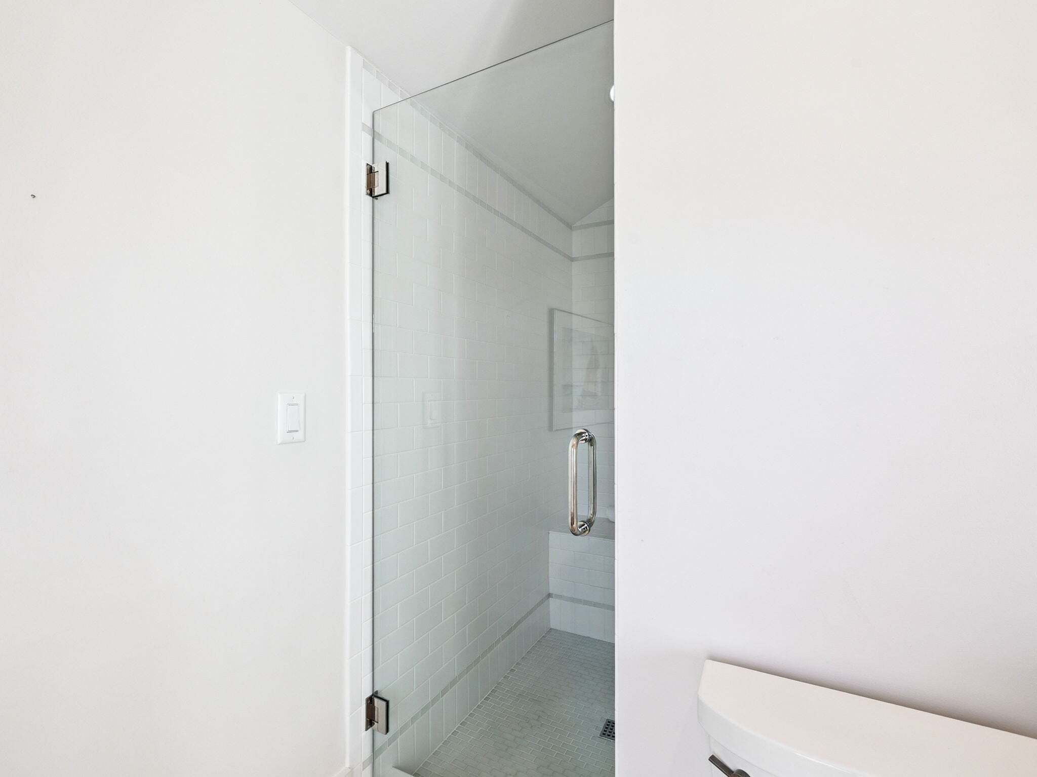 A bathroom with a glass shower door, white tiled walls, and a white toilet.