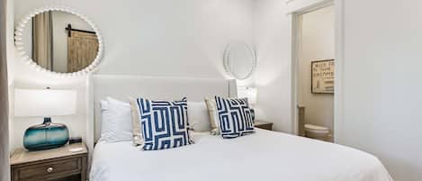 Une chambre à coucher comprenant un lit, deux tables de chevet, une commode, un miroir et un mur orné d’une citation encadrée.