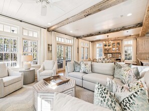 A spacious living room with a large sofa, armchairs, and a coffee table. There are multiple windows providing natural light and a view of the outdoors. - SOUTH of 30A in WaterColor on Park Row! Loaded! (Santa Rosa Beach)