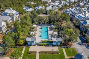 An aerial view of a residential area with a central swimming pool surrounded by modern houses, well-maintained lawns, and a clear sky. - SOUTH of 30A in WaterColor on Park Row! Loaded! (Santa Rosa Beach)
