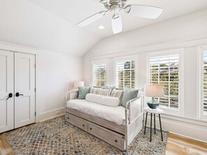 A bedroom with a bed, a ceiling fan, a window with blinds, a small table with a lamp, and a patterned rug. - SOUTH of 30A in WaterColor on Park Row! Loaded! (Santa Rosa Beach)