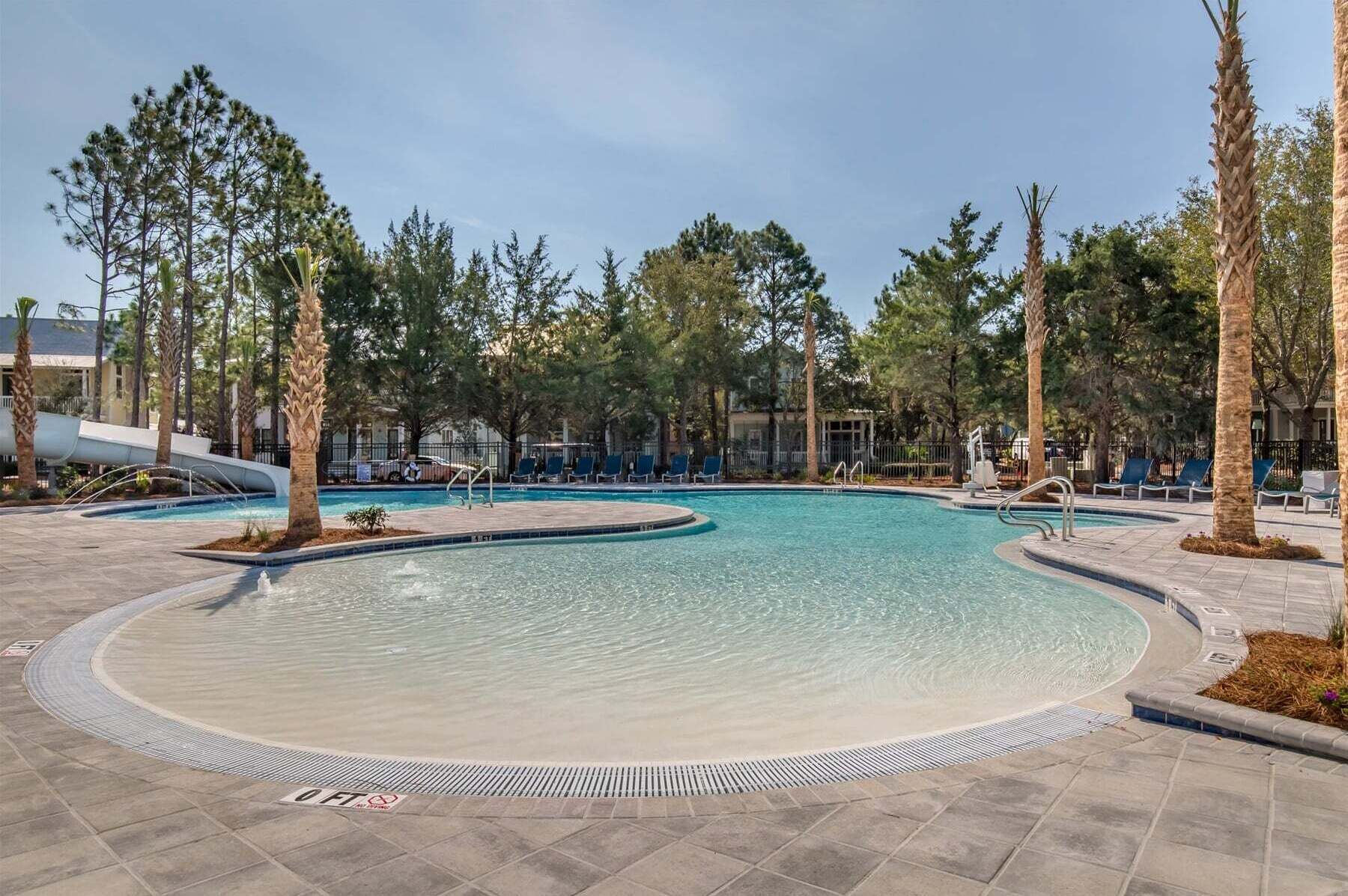 Una piscina a forma circolare, circondata da poltrone prendisole e palme.