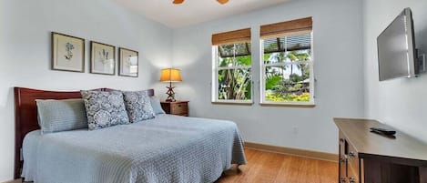 A bedroom with a bed, a ceiling fan, a nightstand, a lamp, a TV, and windows with blinds.