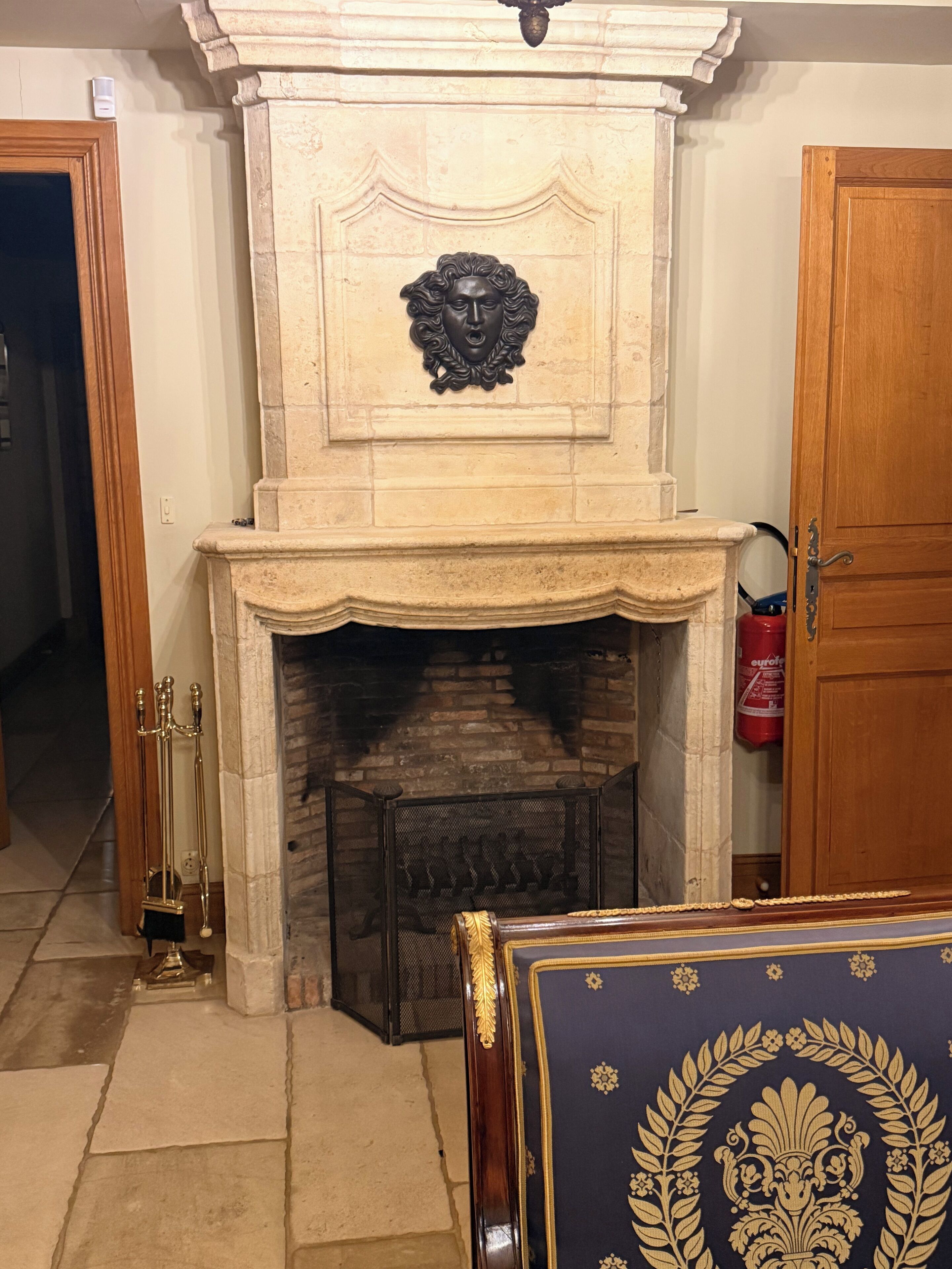 Une cheminée agrémentée d’un manteau décoratif, d’un paravent et d’un chandelier en laiton.