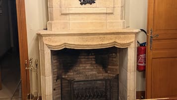 Une cheminée agrémentée d’un manteau décoratif, d’un paravent et d’un chandelier en laiton.