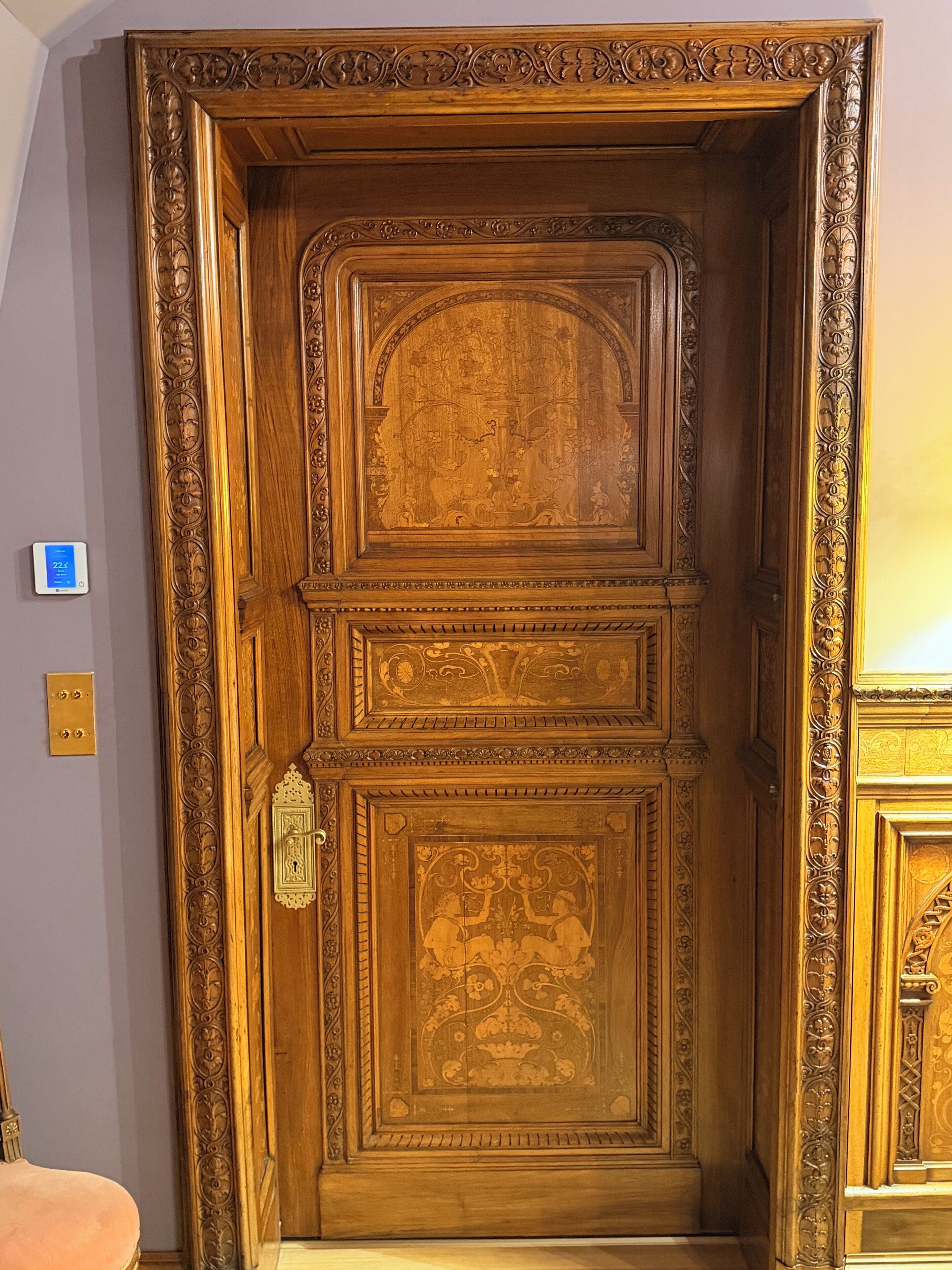 Une porte en bois ornée de sculptures complexes et dotée d’une poignée en laiton.