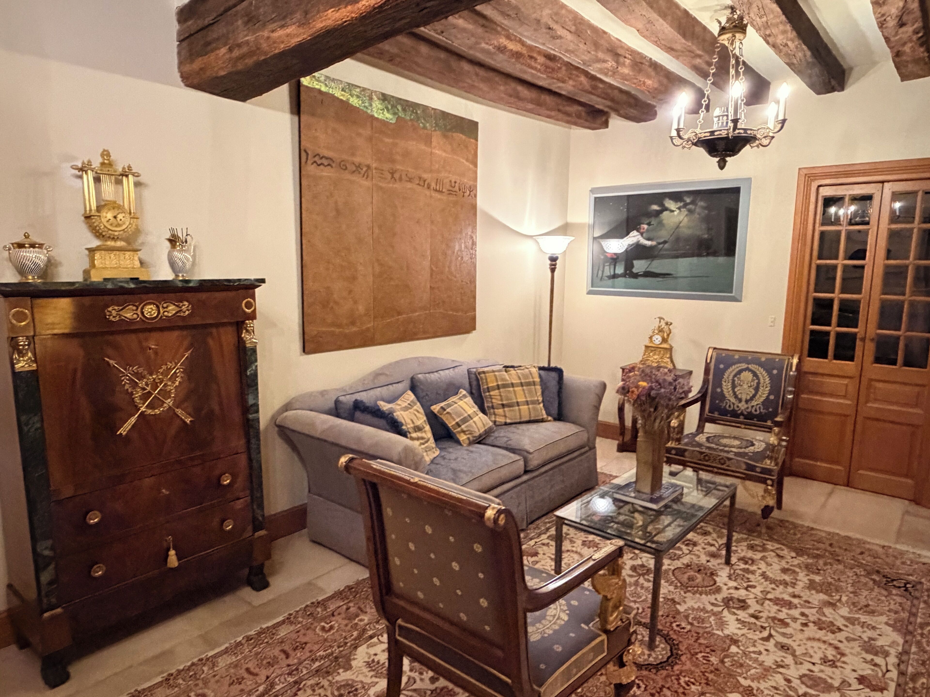 Quarto tradicional com teto de madeira, um sofá, um armário, uma mesa e uma porta.