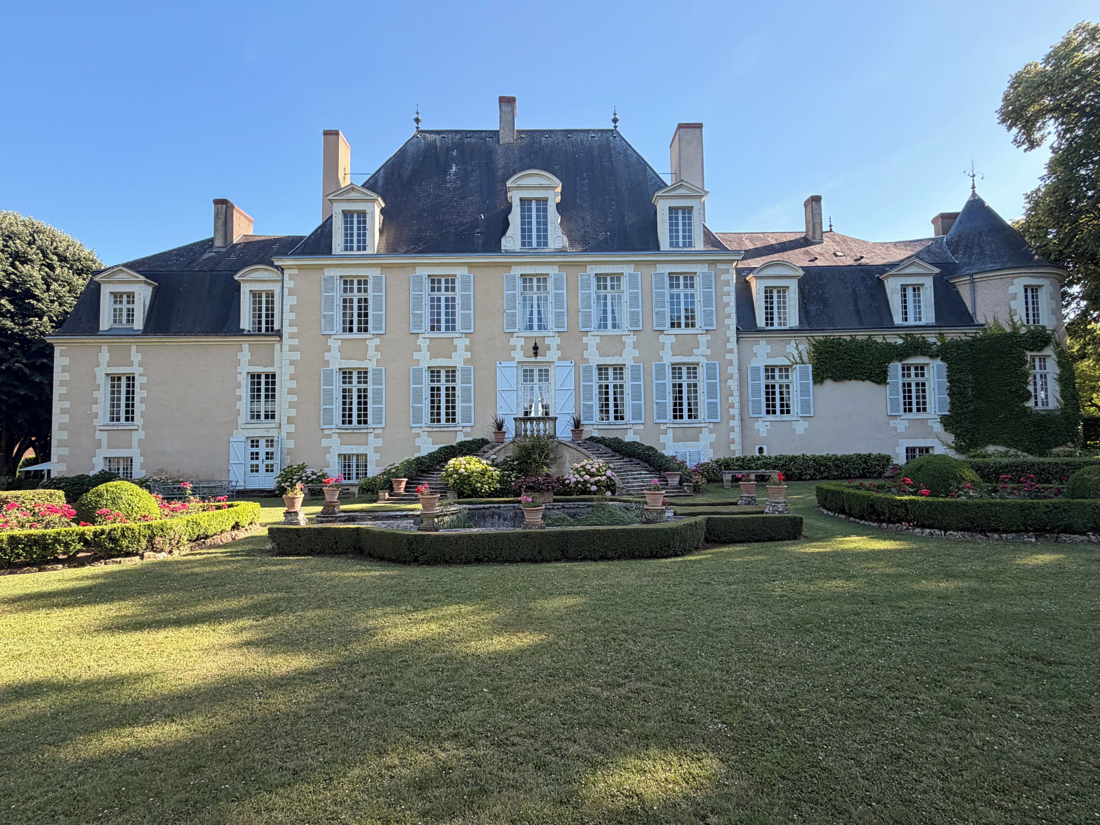 Un grand bâtiment de style classique, doté d’une architecture symétrique, d’un escalier central et d’un jardin bien entretenu.
