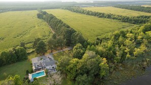 Een groot huis met een zwembad, omgeven door uitgestrekte groene velden en dicht bos.