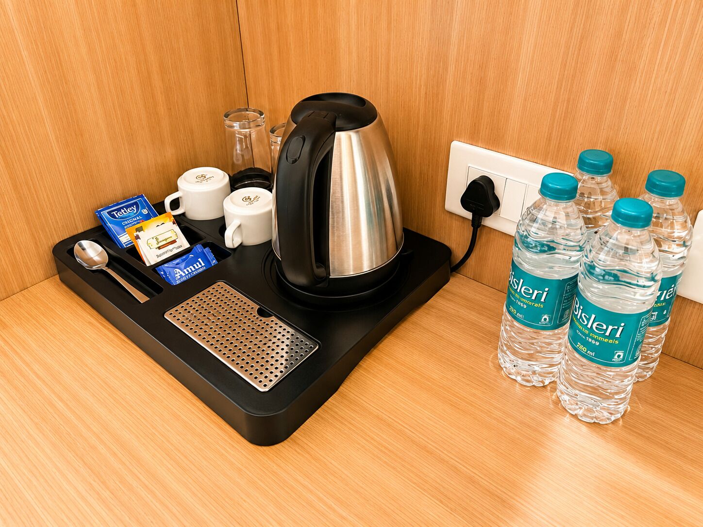A hotel room's breakfast trolley with a kettle, cups, a spoon, a small dish, and Bisleri water bottles.