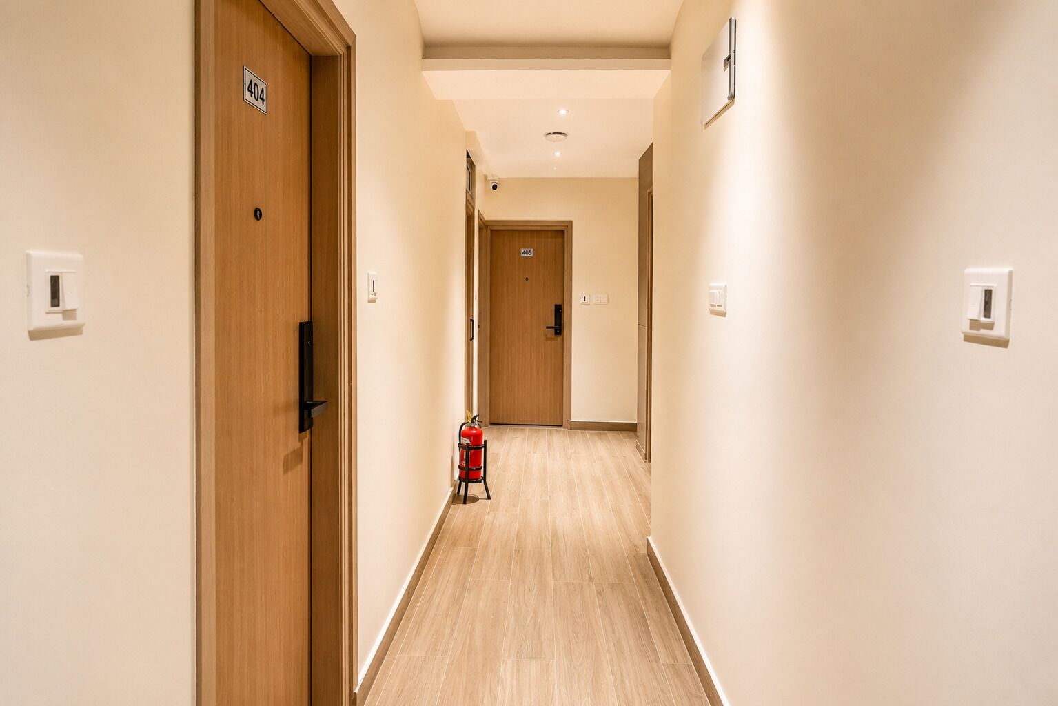 Pasillo de hotel con puertas de madera, un extintor y luces empotradas.