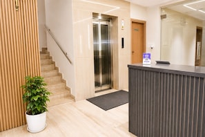A hotel reception area with a reception desk, a staircase, and an elevator. - Axon Bellandur Phase 2 (Bengaluru)