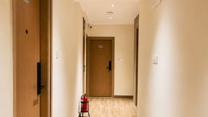 A hotel corridor with wooden doors, a fire extinguisher, and a ceiling with recessed lighting.
