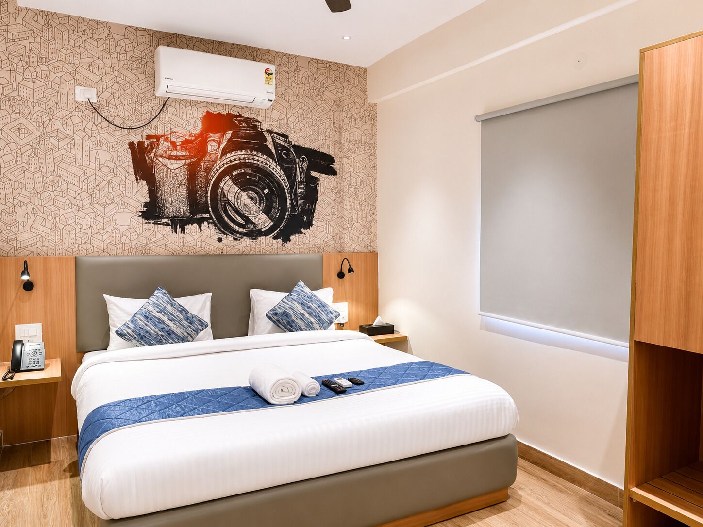 A hotel room with a bed, a wall-mounted air conditioner, a window, and a wooden wardrobe.
