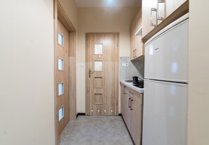 A narrow hallway with wooden doors, a white refrigerator, and a countertop with a coffee maker. - Wilson Park Comfort Apartment (Poznań)