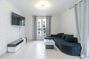 Una sala de estar moderna con un sofá, un televisor montado en la pared y vistas al exterior.