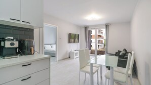 A modern kitchen with a coffee machine, a dining area with a glass table and chairs, and a view of a balcony with a building in the background. - Harmony Park Modern Apartment (Chorzów)
