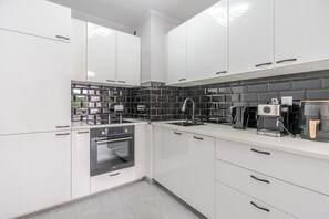 Una cocina moderna con armarios blancos, protector contra salpicaduras negro y electrodomésticos de acero inoxidable.