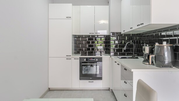 A modern kitchen with white cabinetry, a black tiled backsplash, and stainless steel appliances. - Harmony Park Modern Apartment (Chorzów)