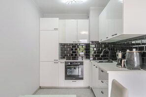 Een moderne keuken met witte kastjes, een zwart betegelde achterwand en roestvrijstalen apparatuur.