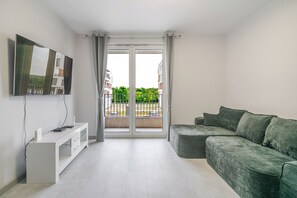 Ein modernes Wohnzimmer mit Flachbildfernseher, einem grauen Sofa und einer Glastür, die auf einen Balkon führt.