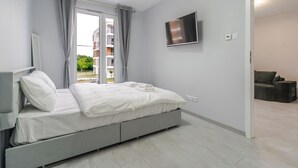 A modern bedroom with a bed, a television, and a view of the outside. - Harmony Park Modern Apartment (Chorzów)