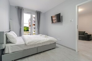 A modern bedroom with a bed, a television, and a view of the outside. - Harmony Park Modern Apartment (Chorzów)