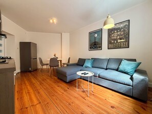 Ein modernes Wohnzimmer mit einem grauen Ecksofa, einem kleinen runden Tisch und einem Essbereich mit weißem Tisch und Stühlen.