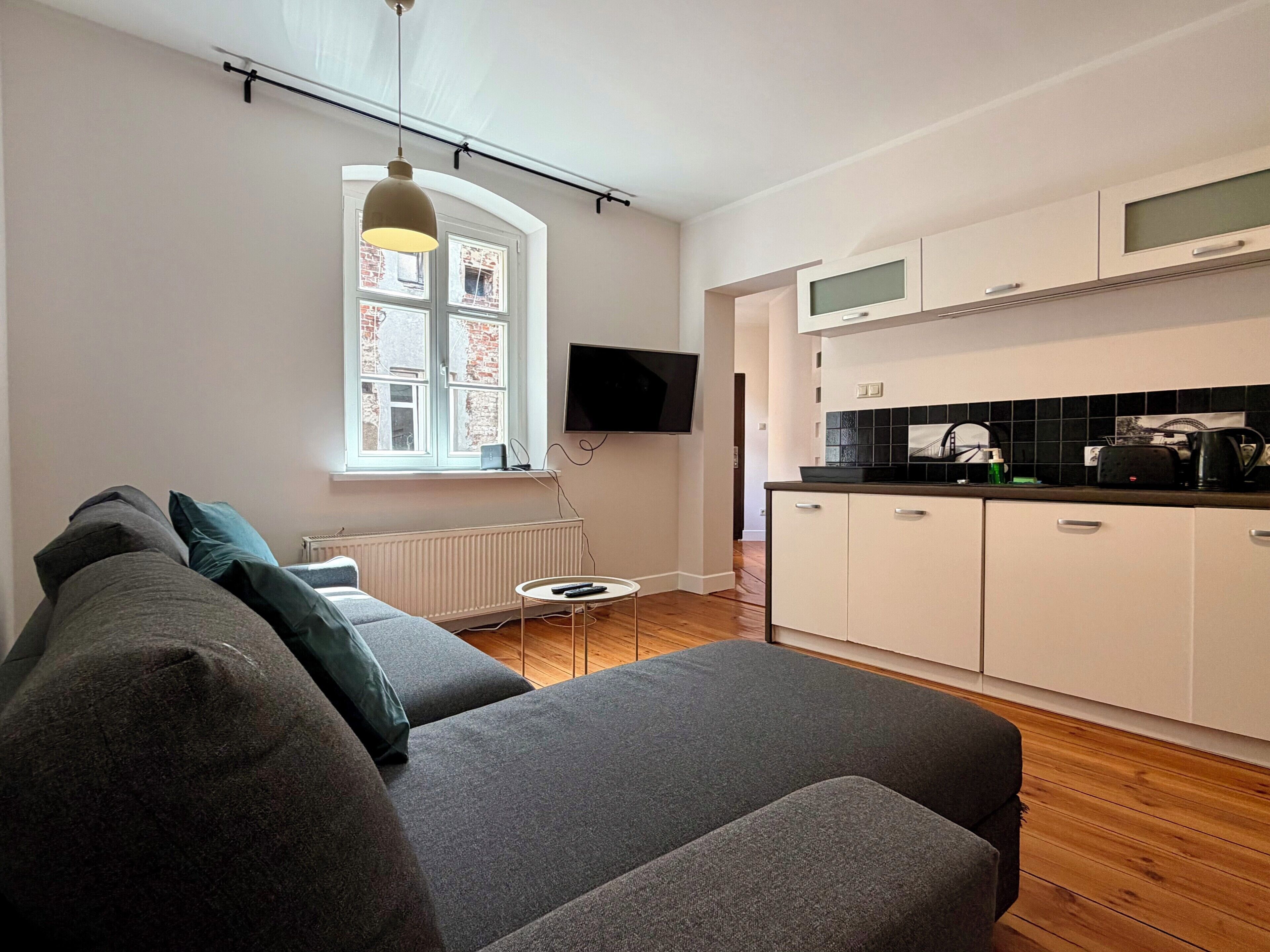 A modern living room with a grey sofa, a small round table, and a television mounted on the wall.