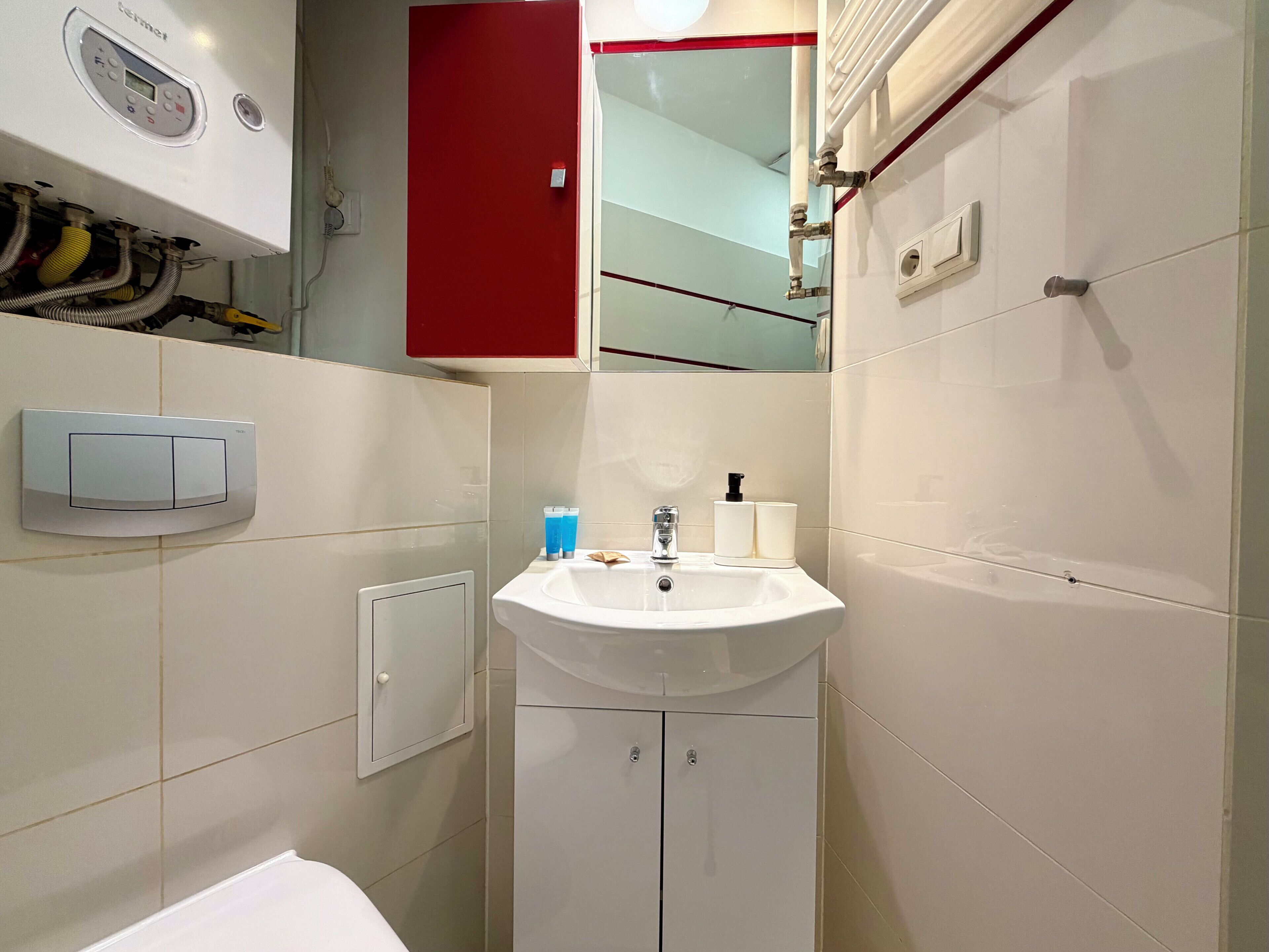Un baño con un lavamanos blanco, un armario rojo y un espejo.