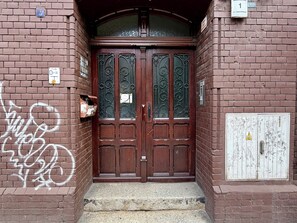 Eine braune Holztür mit dekorativen Glasfeldern, eine Ziegelwand mit Graffiti und ein kleiner Briefkasten.