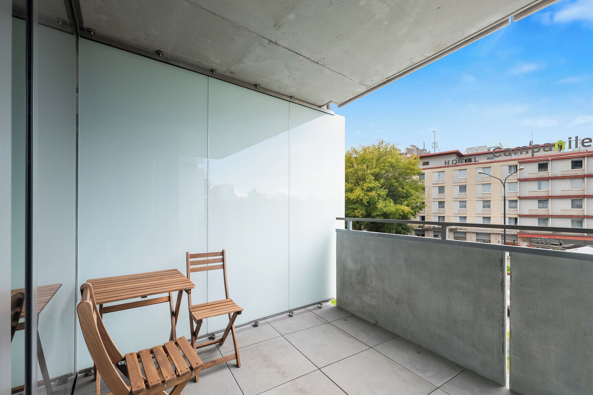 Un balcon doté d’une paroi en verre, d’une table et d’une chaise en bois, et offrant une vue sur un immeuble d’hôtel.