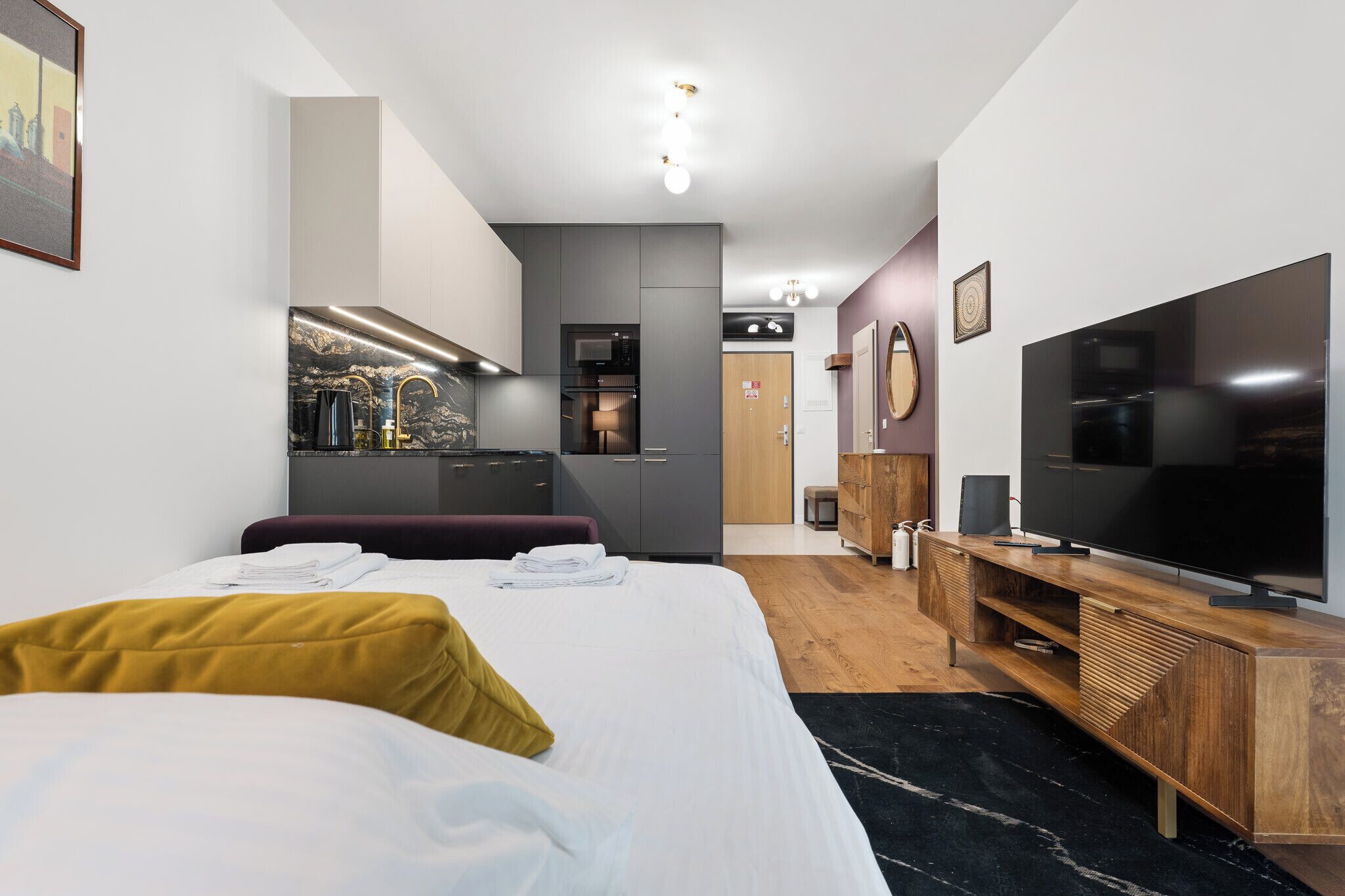 A hotel room with a bed, a TV, a wooden dresser, a microwave, and a small kitchenette.
