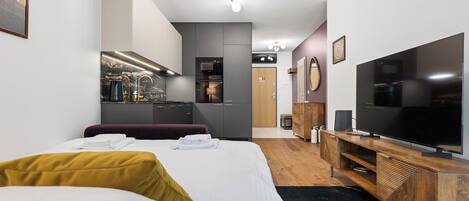 A hotel room with a bed, a TV, a wooden dresser, a microwave, and a small kitchenette.