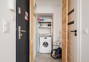 A laundry room with a washing machine, a dryer, and a vacuum cleaner. - Puławska Urban Nest Apartment (Warszawa)