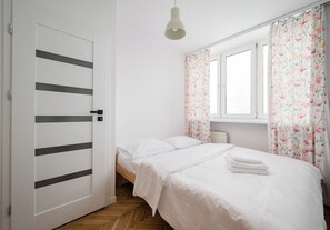 Une chambre à coucher avec un lit, une fenêtre ornée de rideaux à motifs floraux, une lampe de chevet et une porte à rayures horizontales.