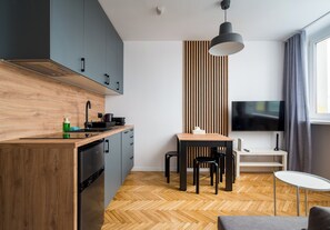 A modern kitchen with a built-in oven, a wooden countertop, and a dining area with a table and chairs. - Puławska Urban Nest Apartment (Warszawa)